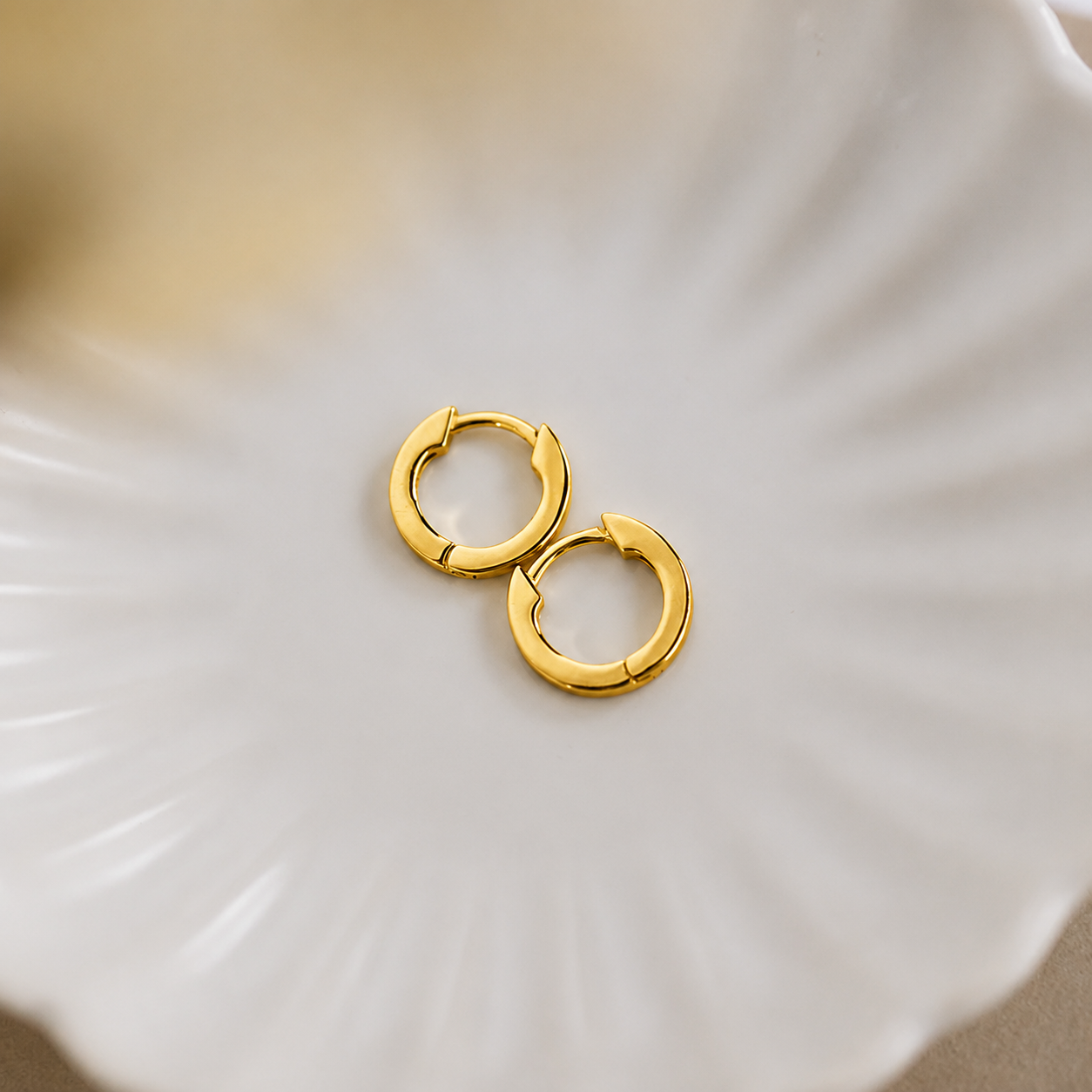 Gold hoop earrings on a white shell
