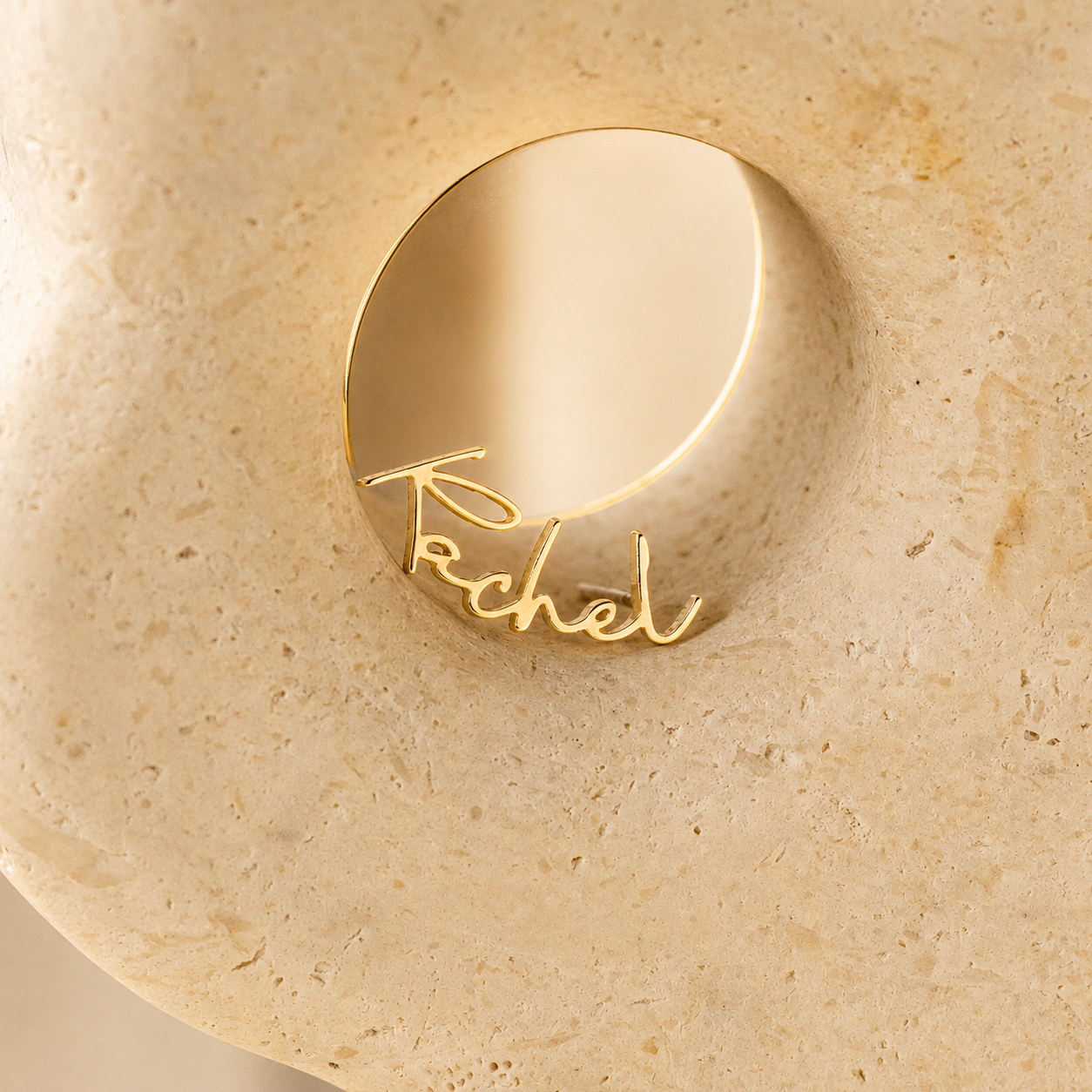 Gold ring with 'Rachel' engraving on a beige stone surface