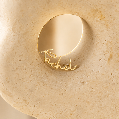 Gold ring with 'Rachel' engraving on a beige stone surface