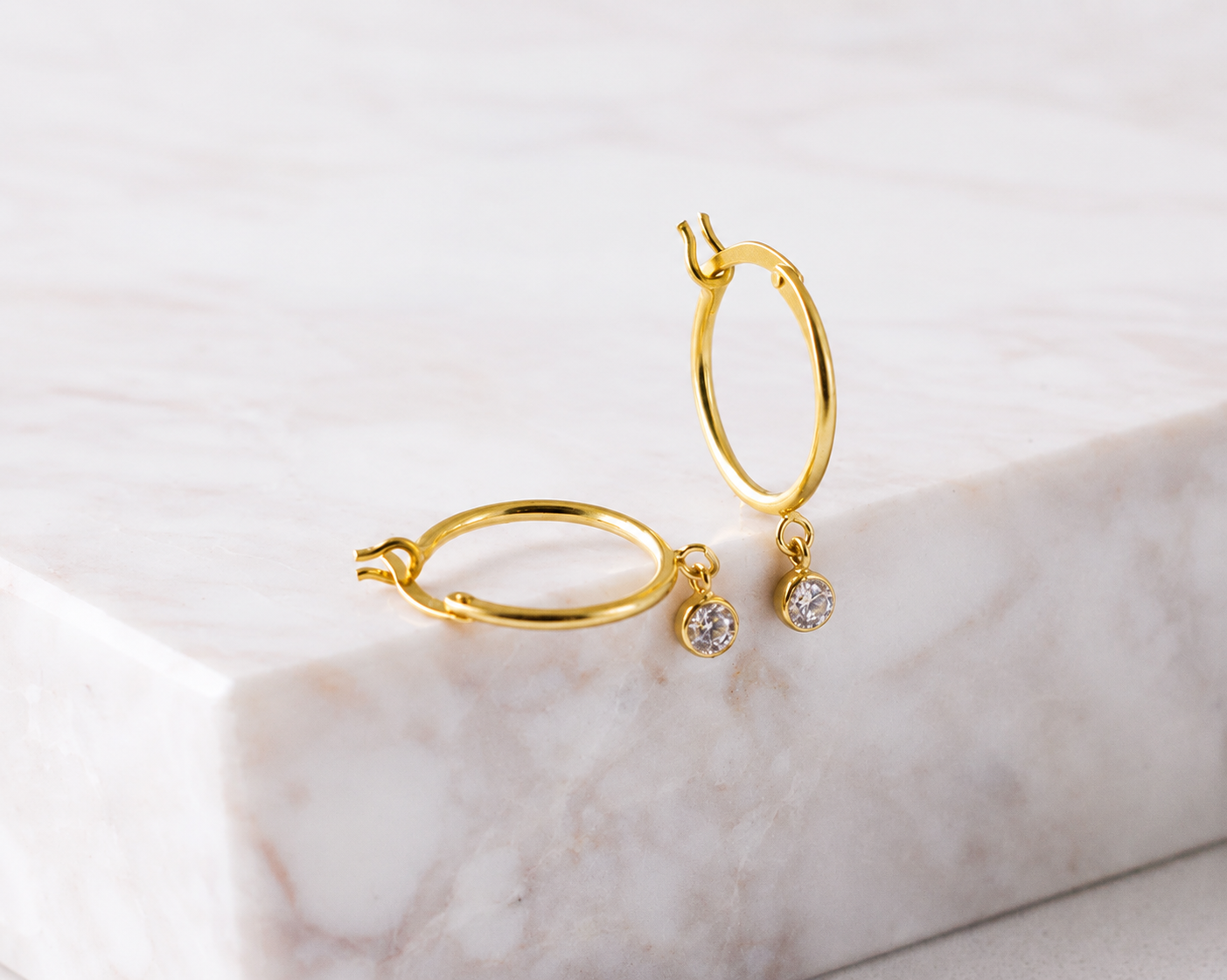 Gold hoop earrings with small round gemstones on a marble surface