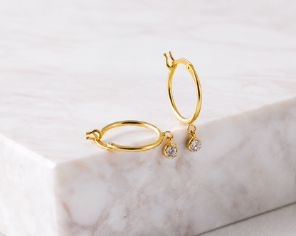 Gold hoop earrings with small round gemstones on a marble surface