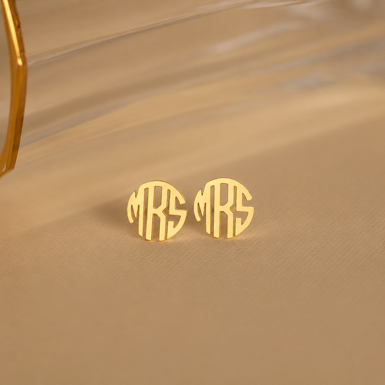Gold monogram earrings on a beige fabric background
