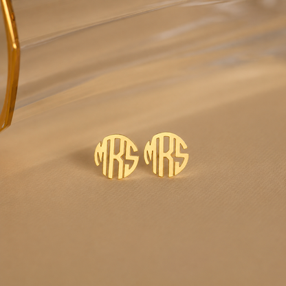 Gold monogram earrings on a beige fabric background