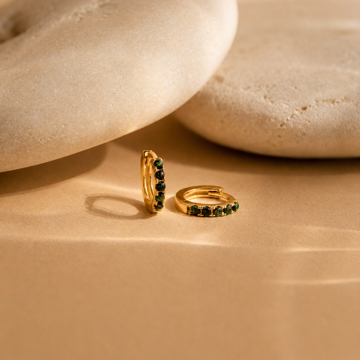 Gold hoop earrings with green gemstones on a beige stone surface