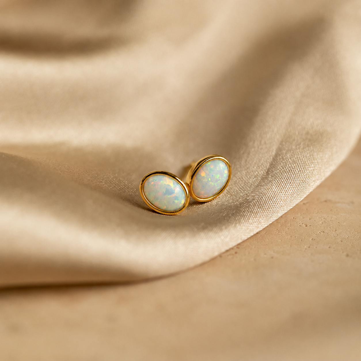 Gold earrings with opal stones on a beige fabric background