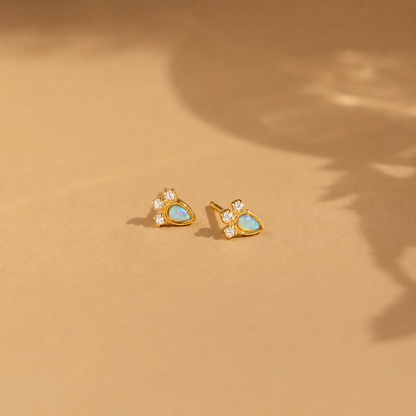 Gold earrings with opal stones on a beige background
