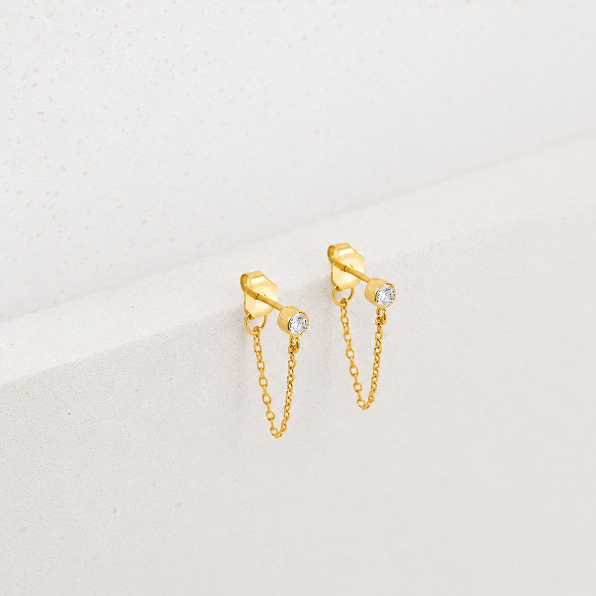 Gold chain earrings with small diamonds on a light gray background