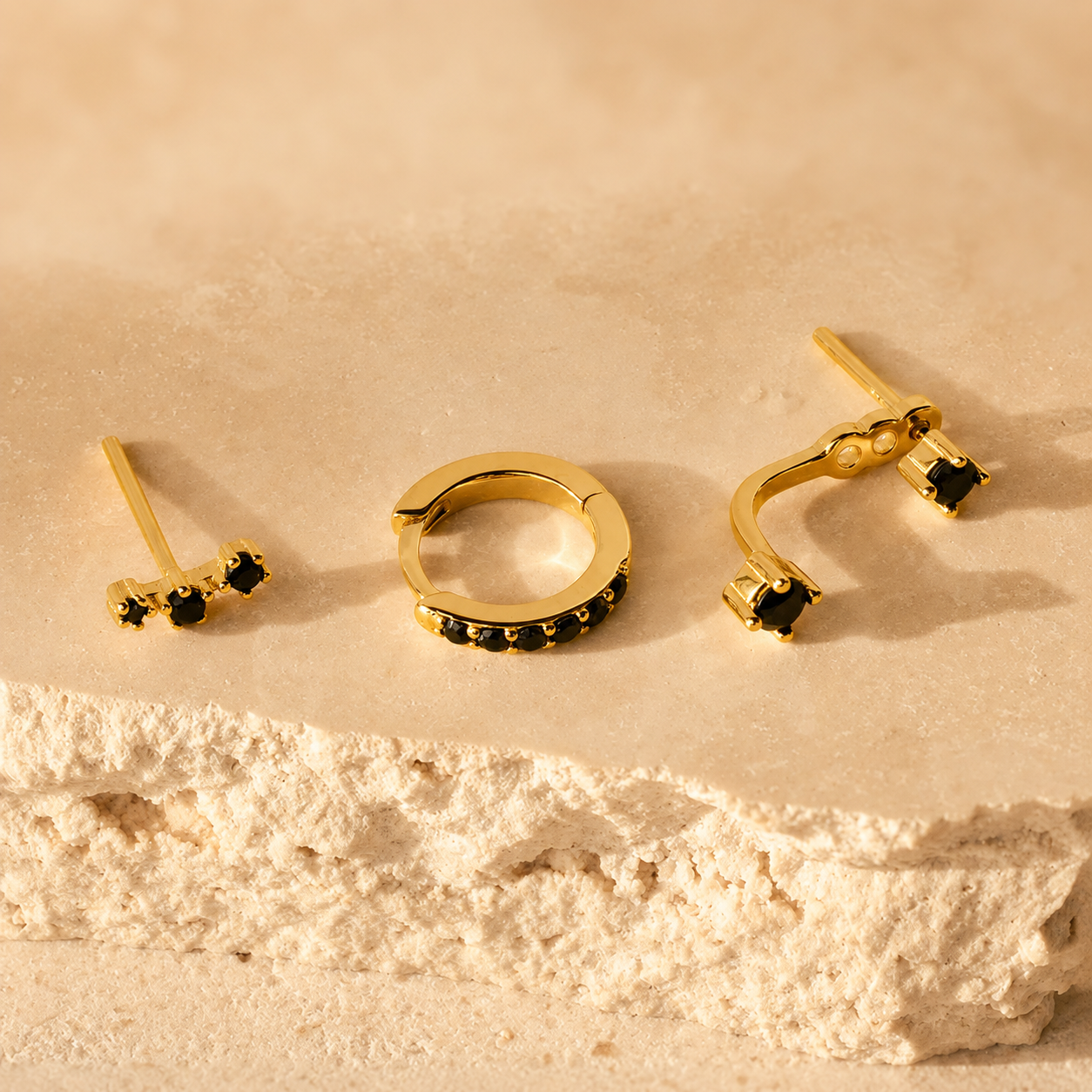 Set of gold earrings with black gemstones on a beige stone surface