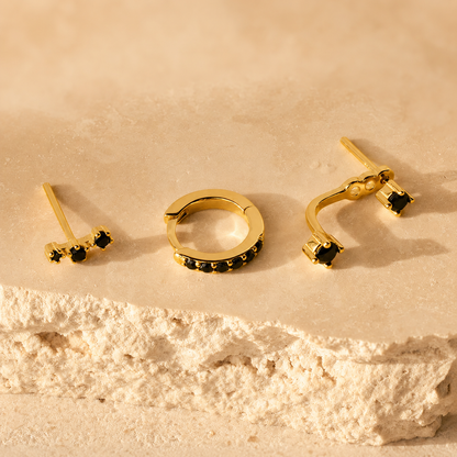 Set of gold earrings with black gemstones on a beige stone surface