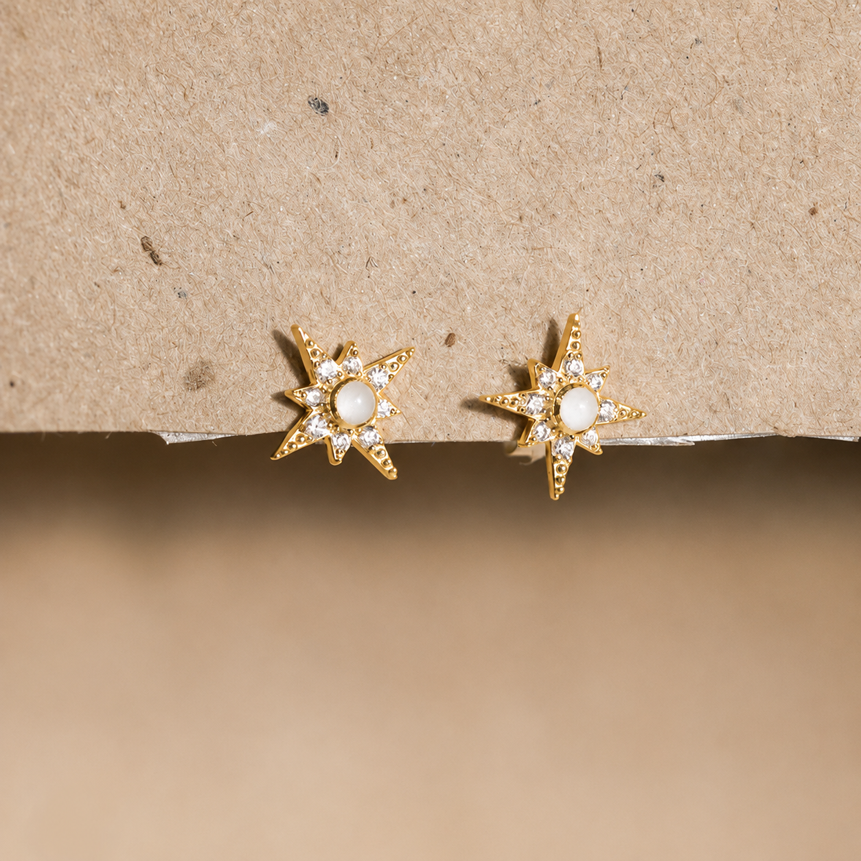Gold star-shaped earrings with clear stones on a beige background
