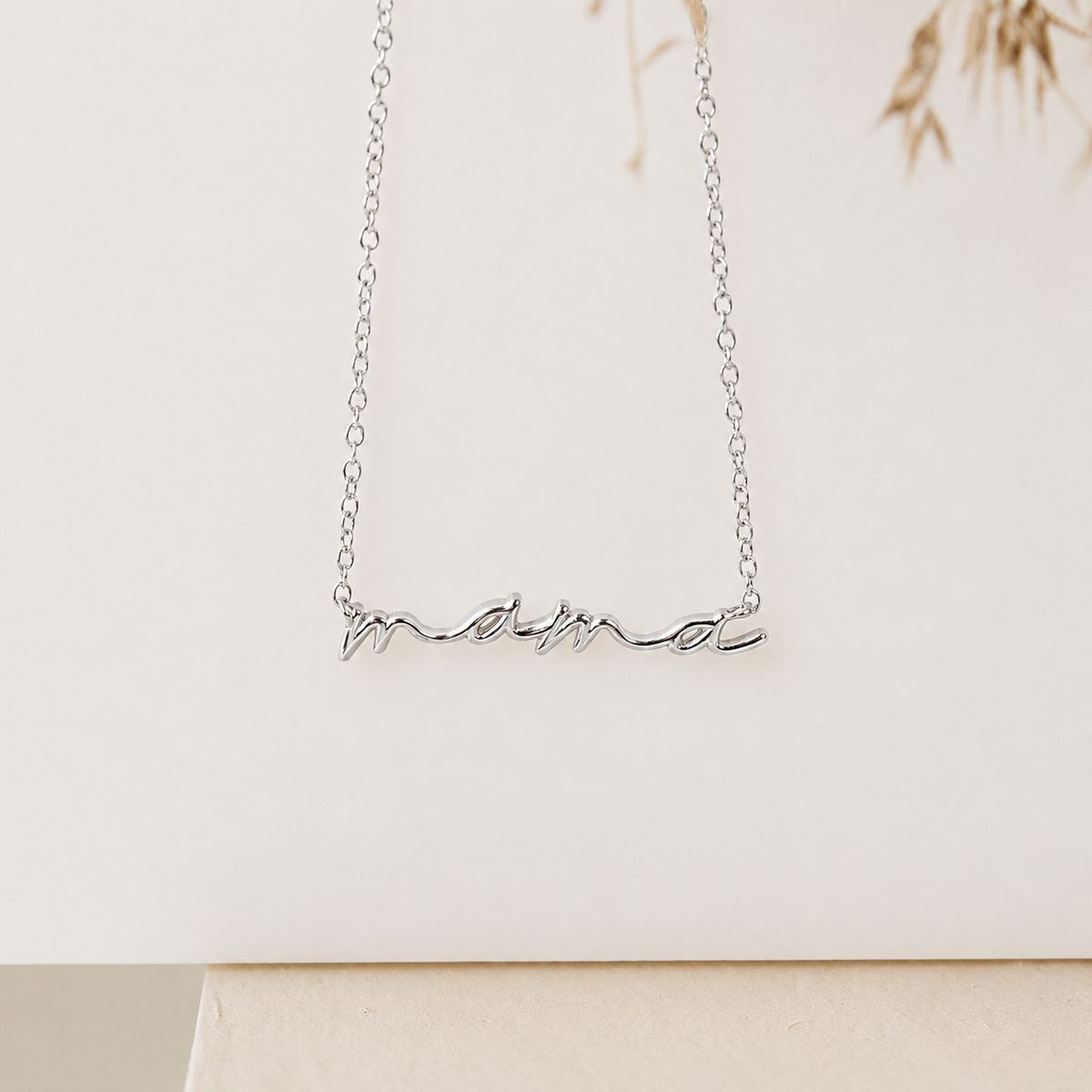 Silver necklace with 'mama' pendant on a light background