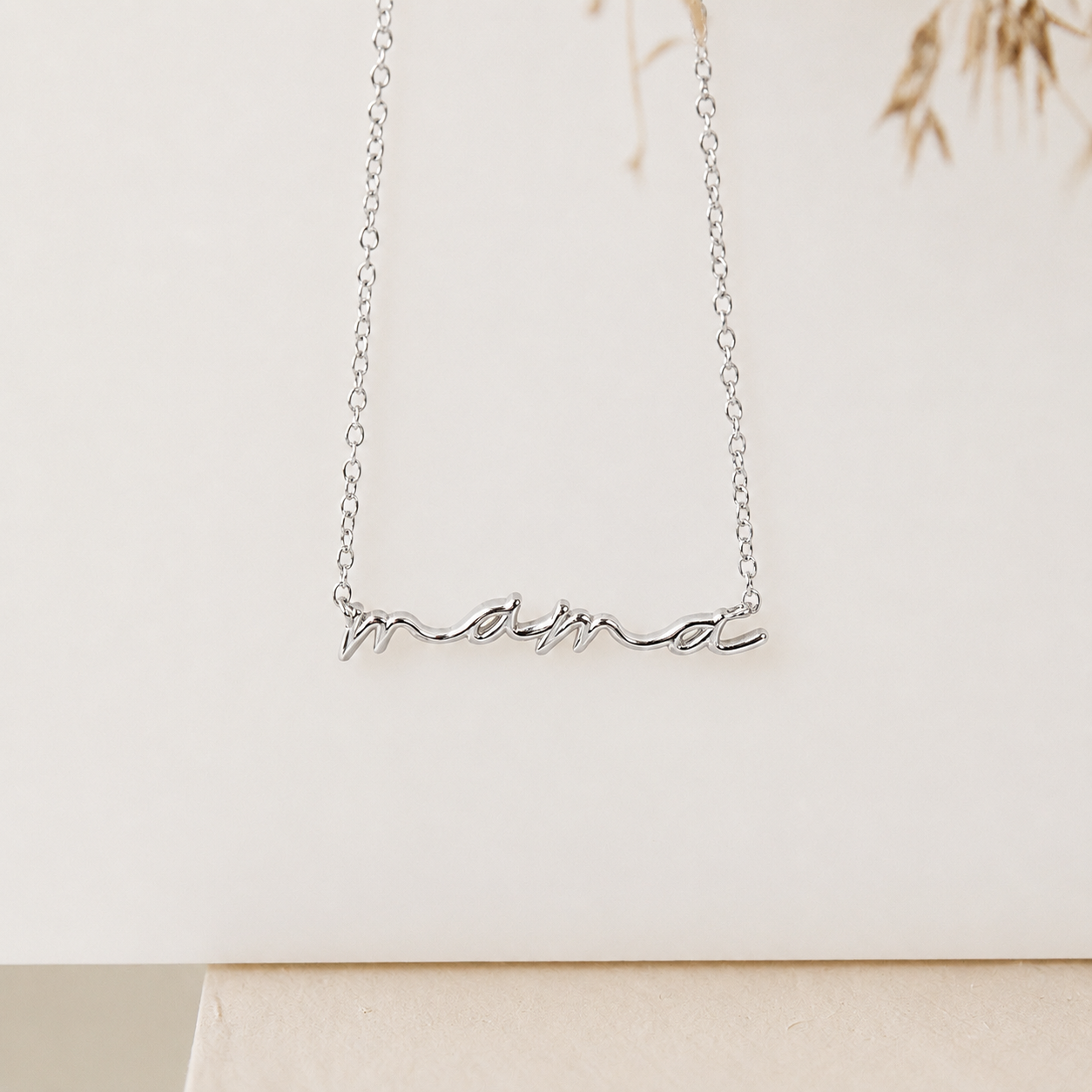 Silver necklace with 'mama' pendant on a light background