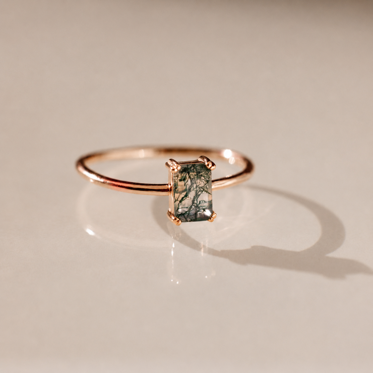 Rose gold ring with a green gemstone on a beige background
