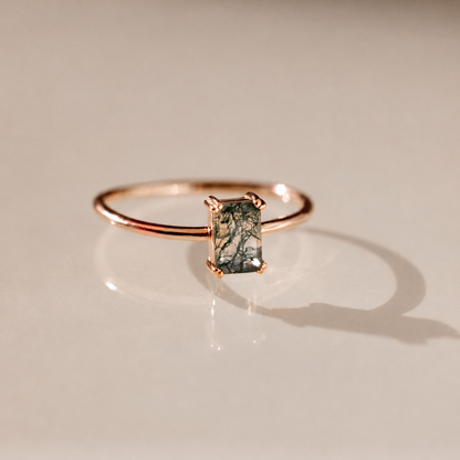 Rose gold ring with a green gemstone on a beige background