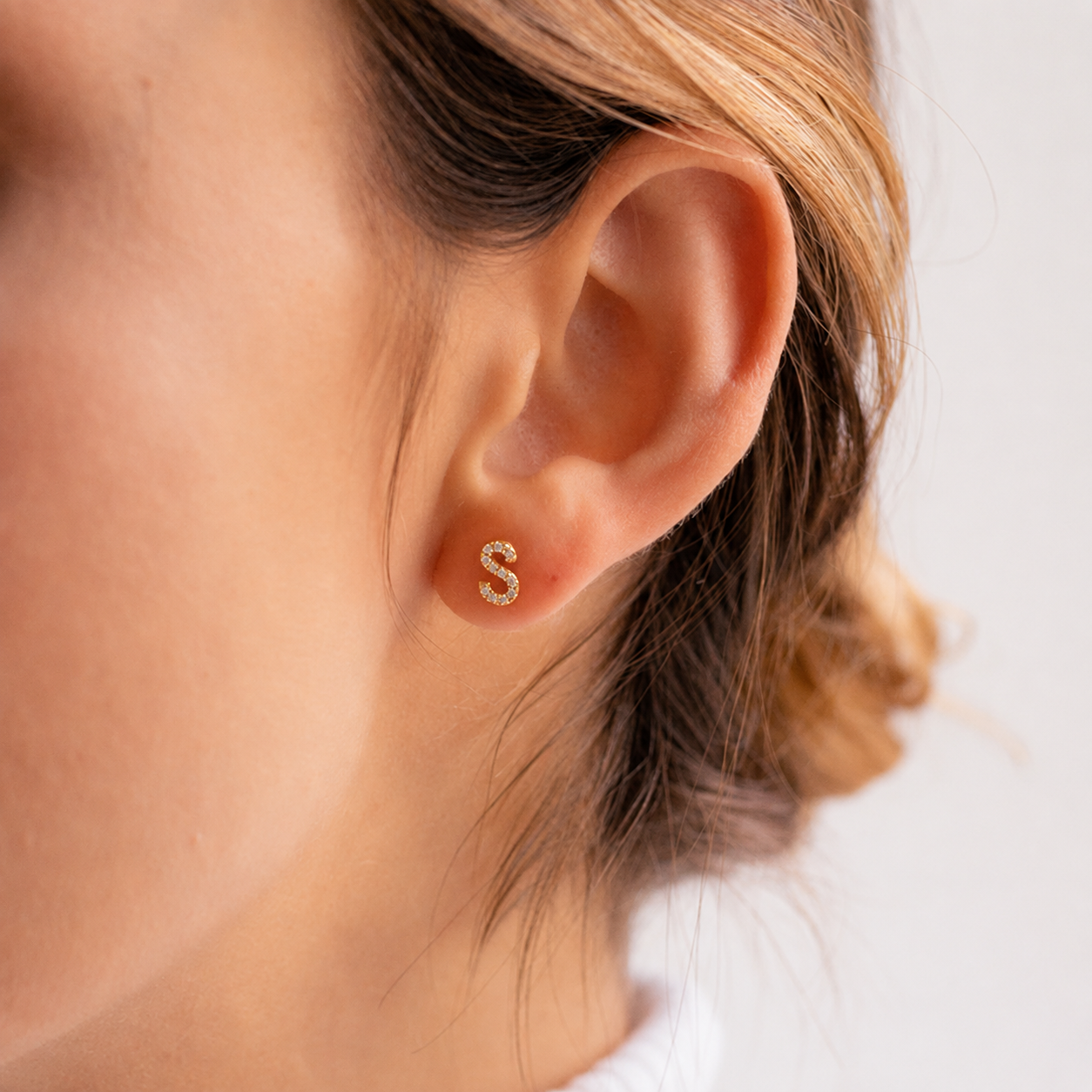 Gold earring with 'S' detail on a person's ear against a neutral background