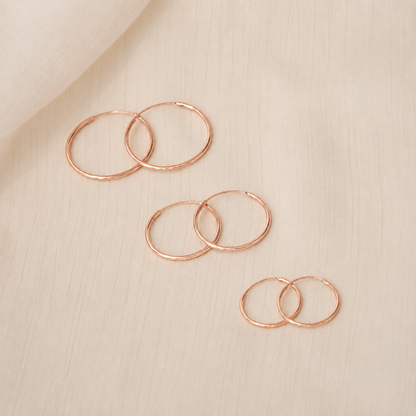 Set of rose gold hoop earrings on a beige fabric background