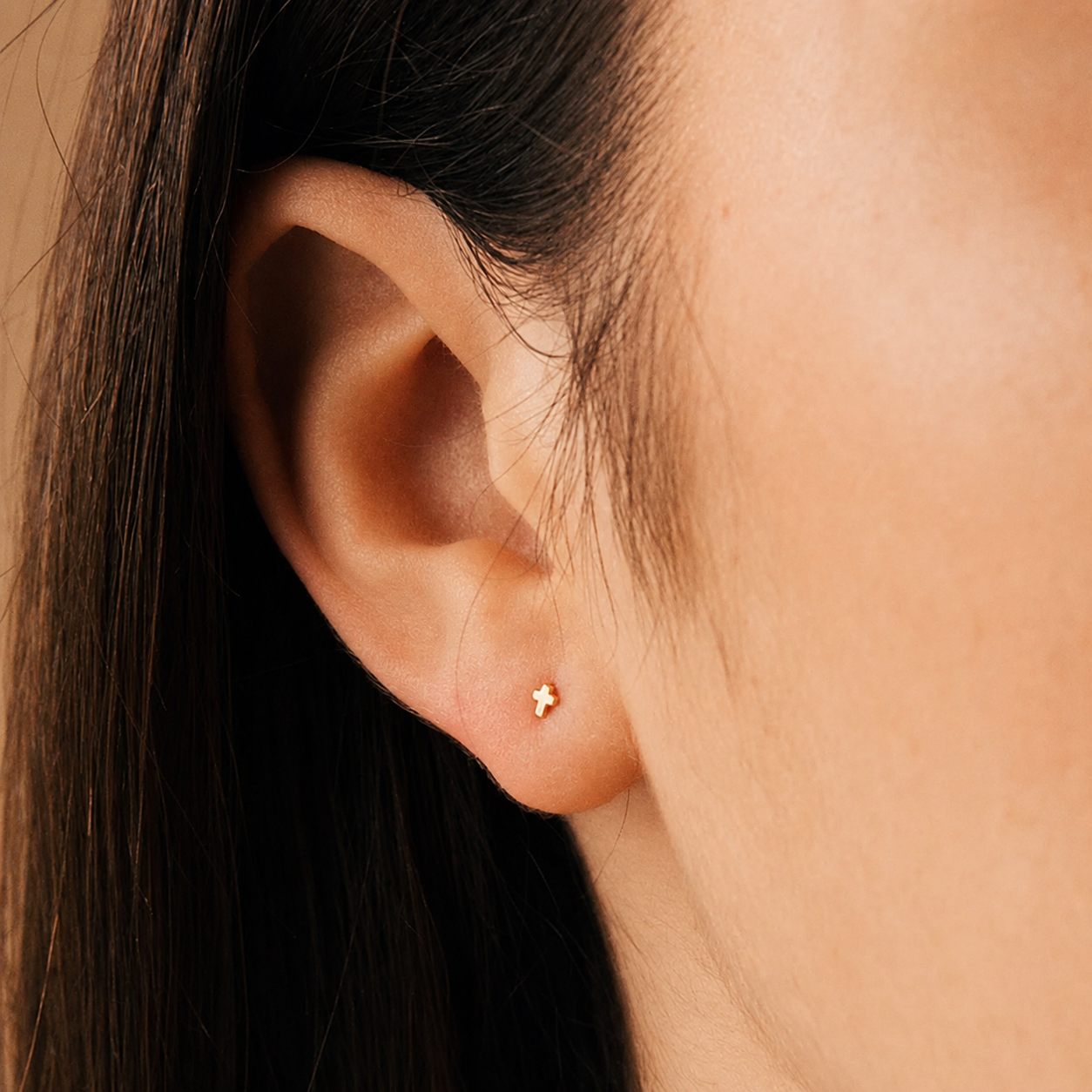 Close-up of an ear wearing a small gold earring with a cross detail.