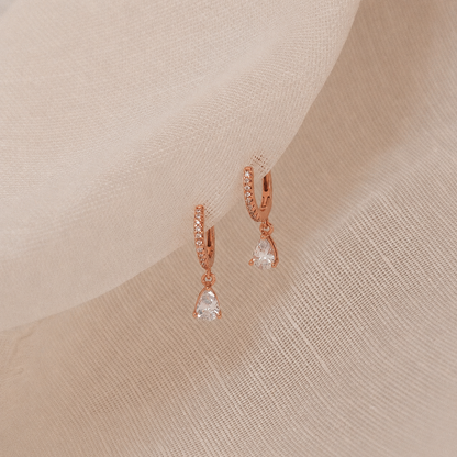 Rose gold earrings with clear gemstones on a beige fabric background