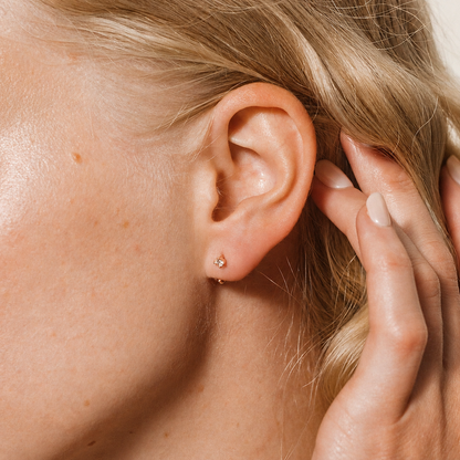 Close-up of a person's ear with a small earring, hand touching hair