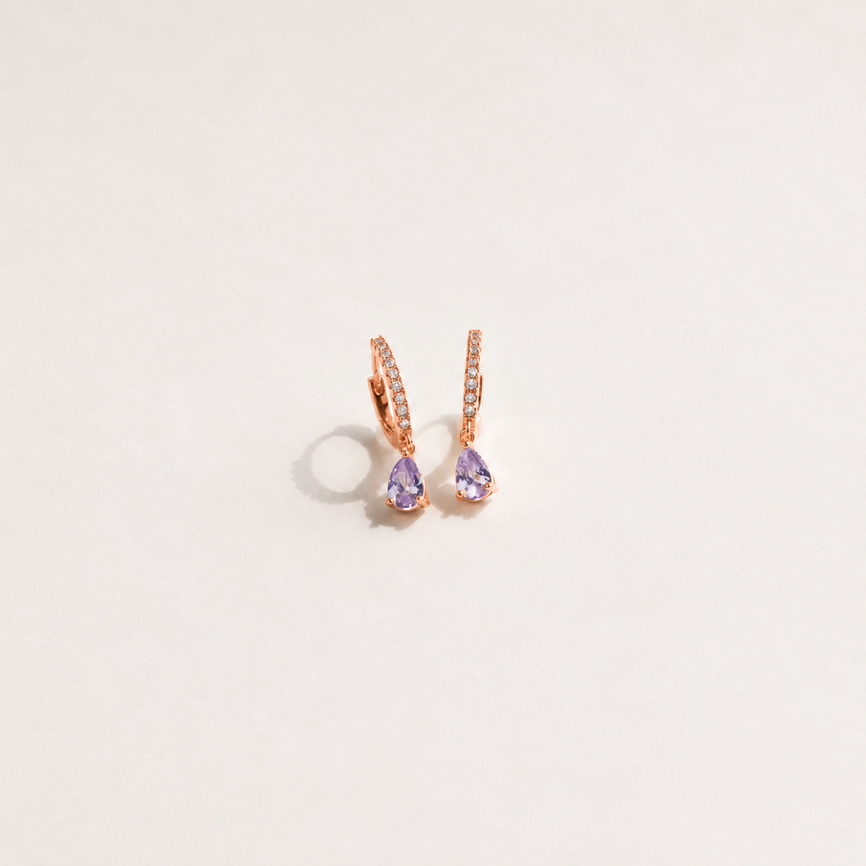 Rose gold earrings with purple gemstones on a light gray background