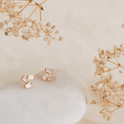 Rose gold earrings with clear stones on a light beige background with dried flowers.
