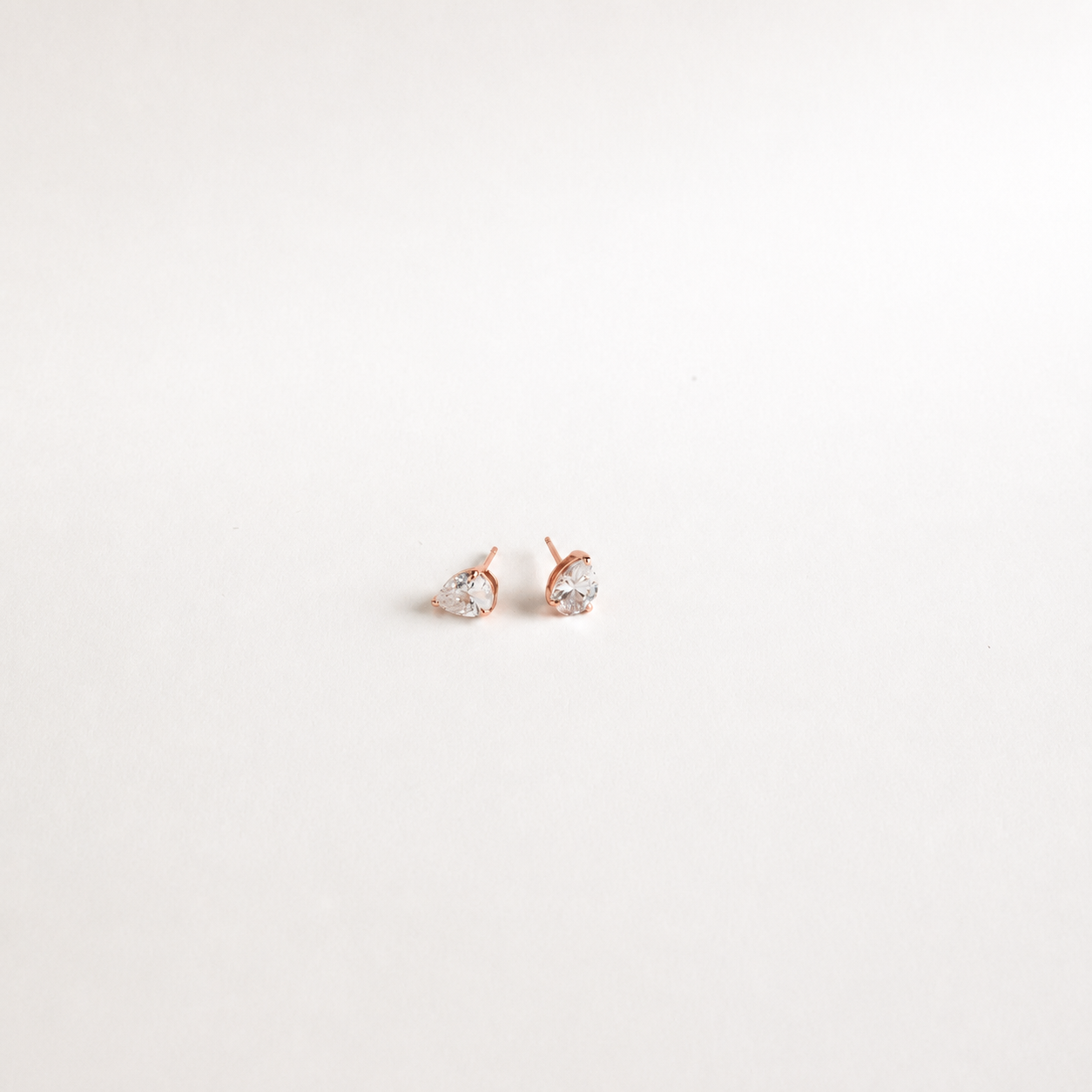 A pair of small rose gold stud earrings with clear teardrop-shaped gemstones, set against a plain white background.