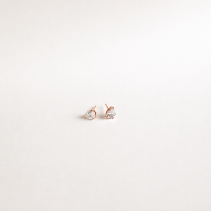 A pair of small rose gold stud earrings with clear teardrop-shaped gemstones, set against a plain white background.
