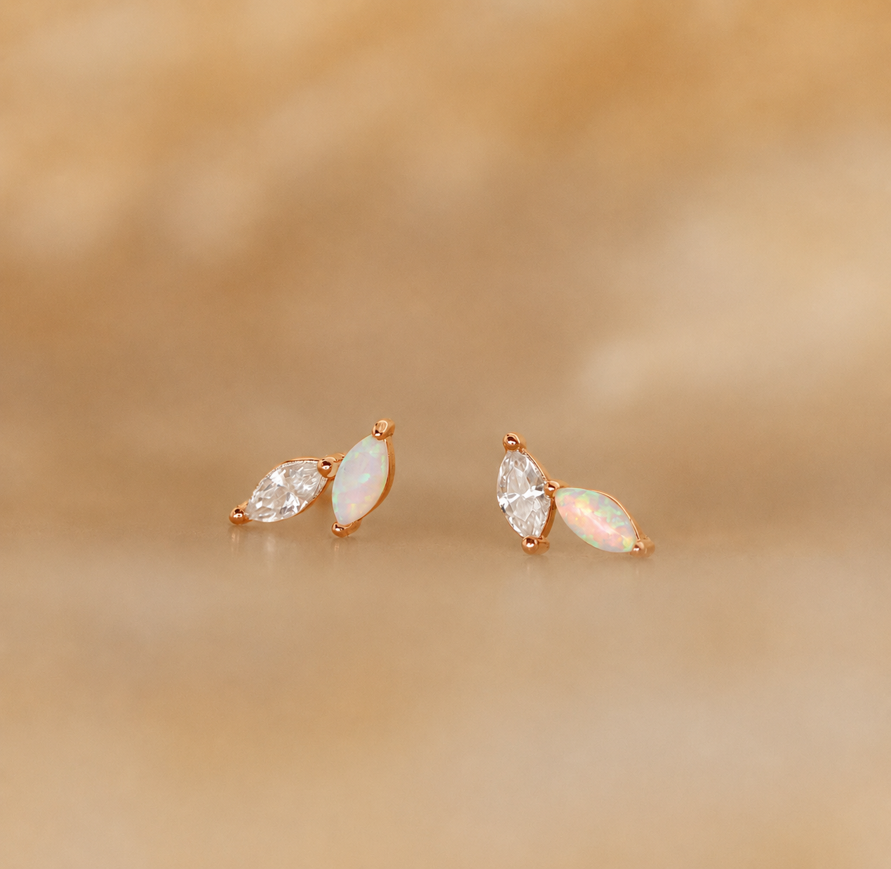 Pair of gold earrings with opal and clear gemstones on a beige background