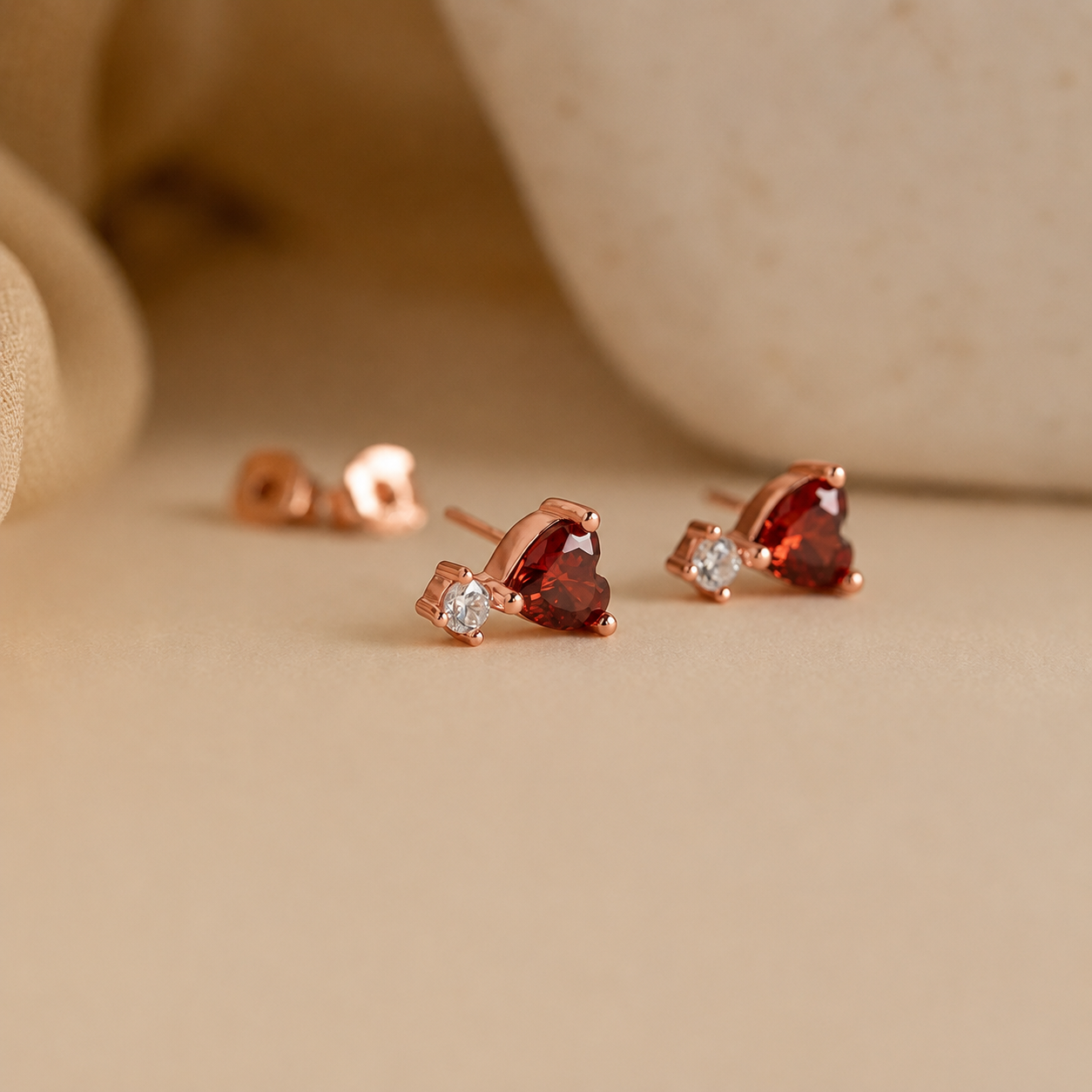Heart-shaped gemstone earrings with rose gold setting on a beige background