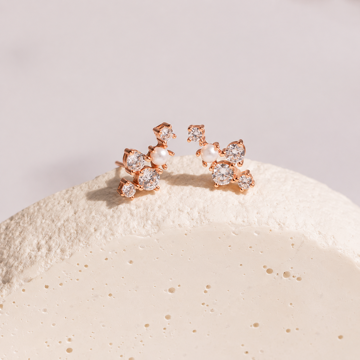 Rose gold earrings with clear gemstones on a textured beige surface