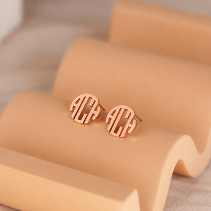 Rose gold monogram earrings on a beige surface