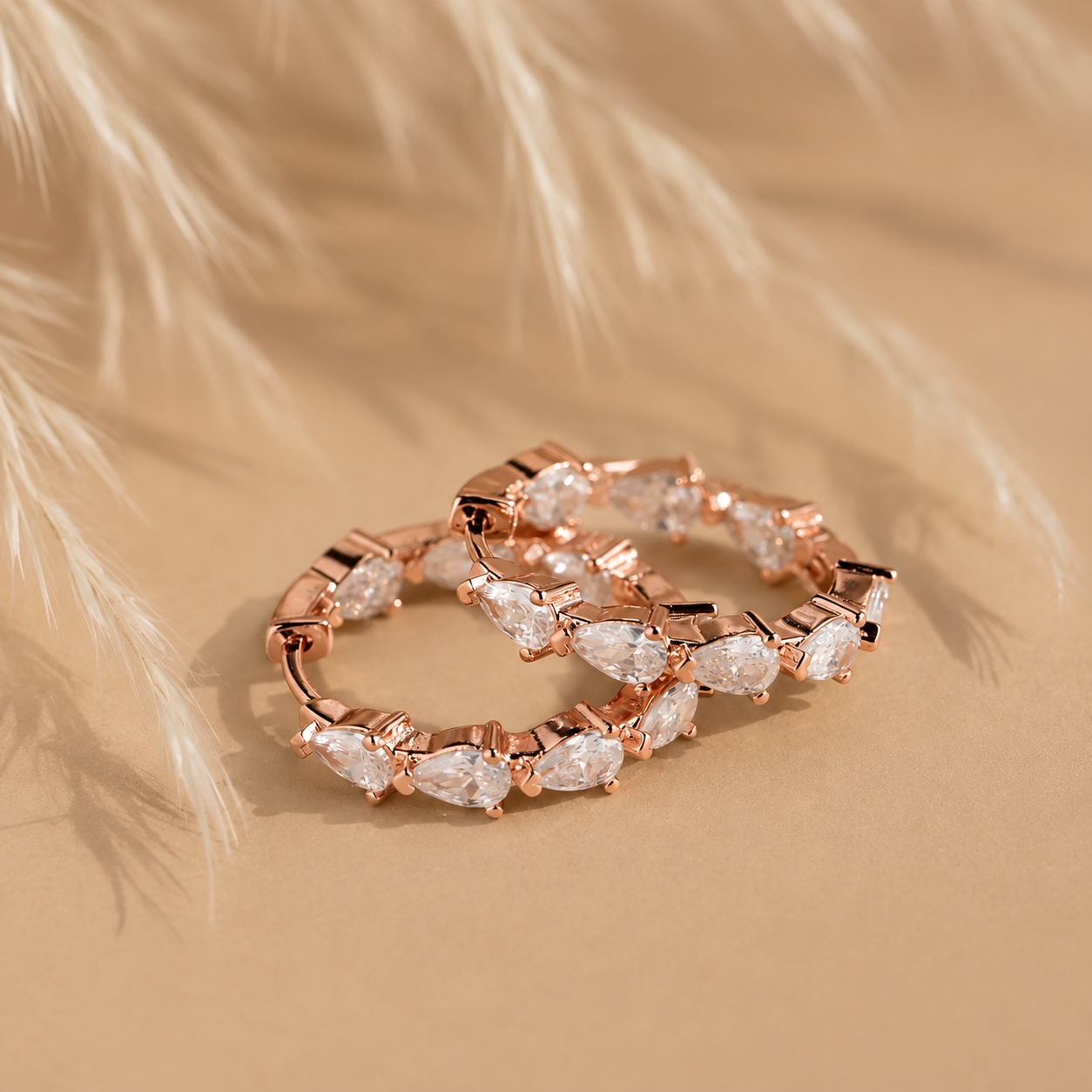 Rose gold hoop earrings with clear gemstones on a beige background