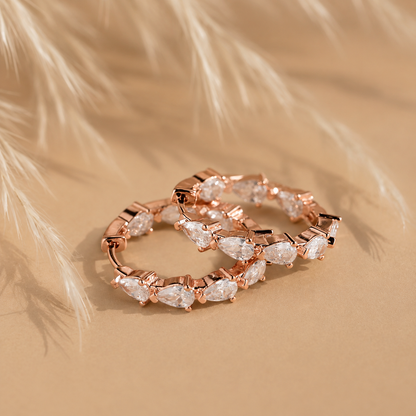 Rose gold hoop earrings with clear gemstones on a beige background