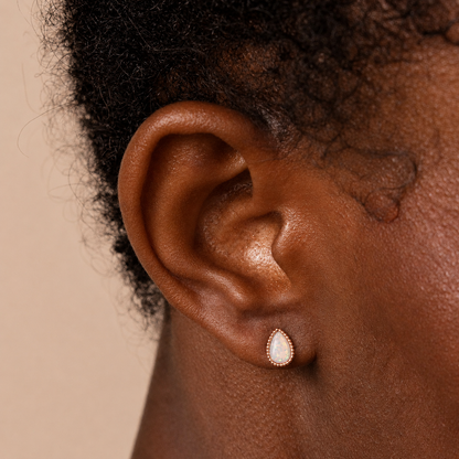 Close-up of an ear wearing a teardrop earring on a beige background