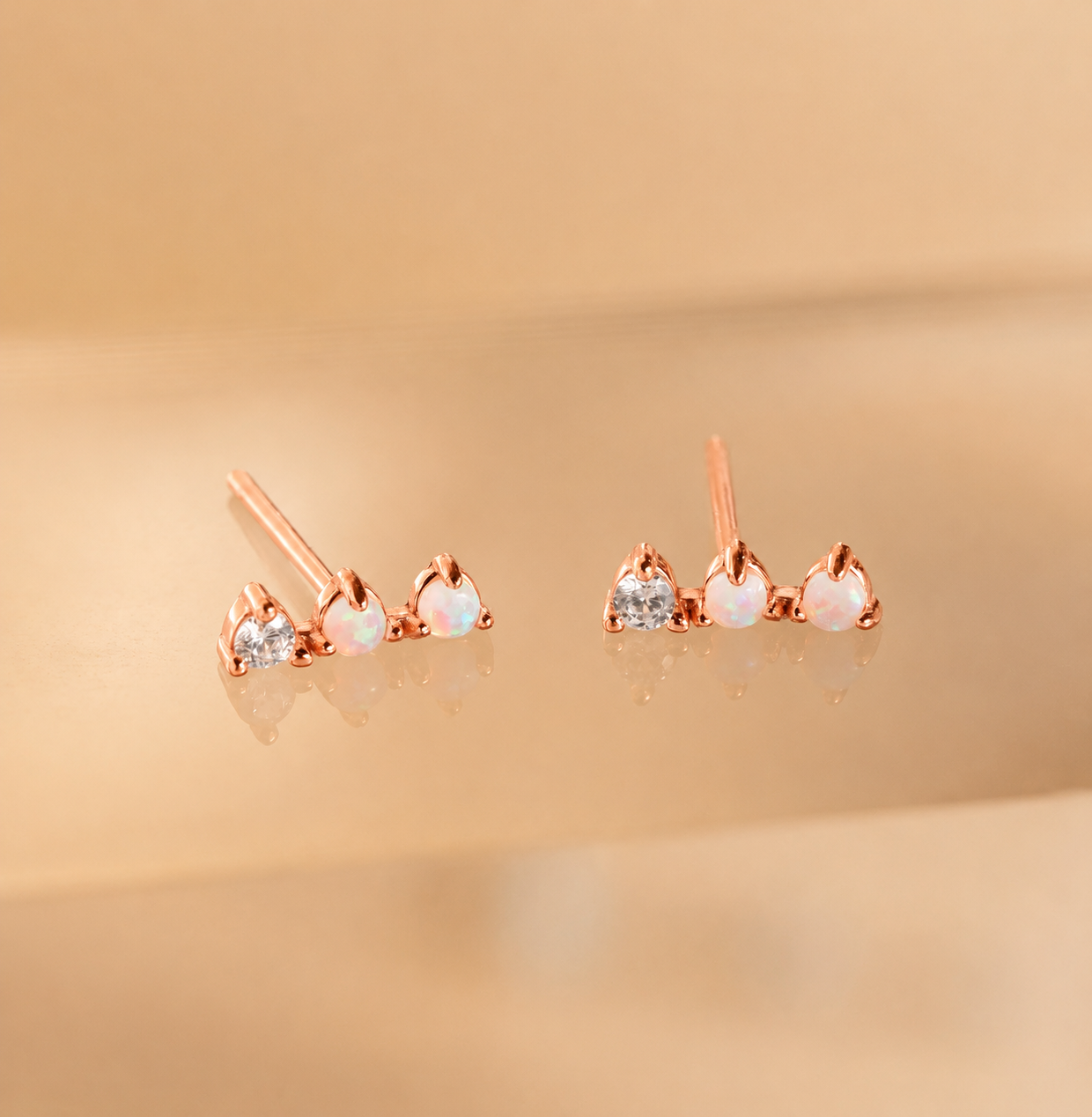 Rose gold earrings with opal and clear gemstones on a beige background