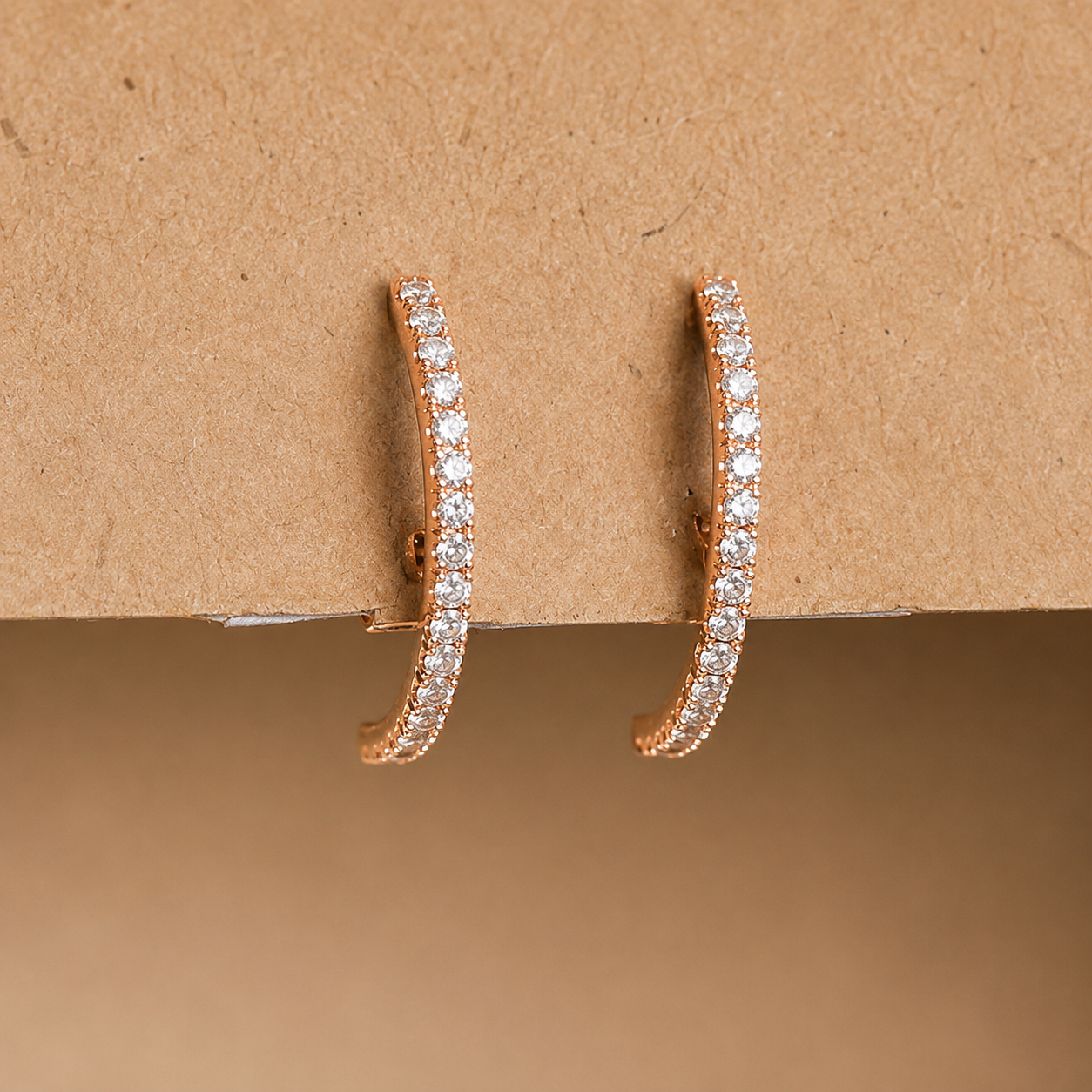 Rose gold hoop earrings with clear stones on a brown background
