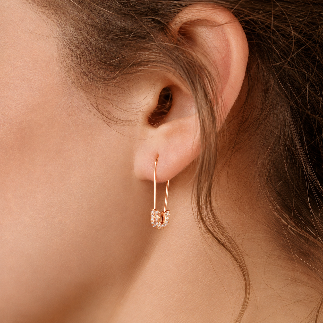 Close-up of an ear wearing a rose gold hoop earring with small diamonds.