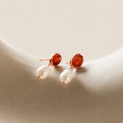 Pair of earrings with pearl-like stones and rose gold accents on a beige background