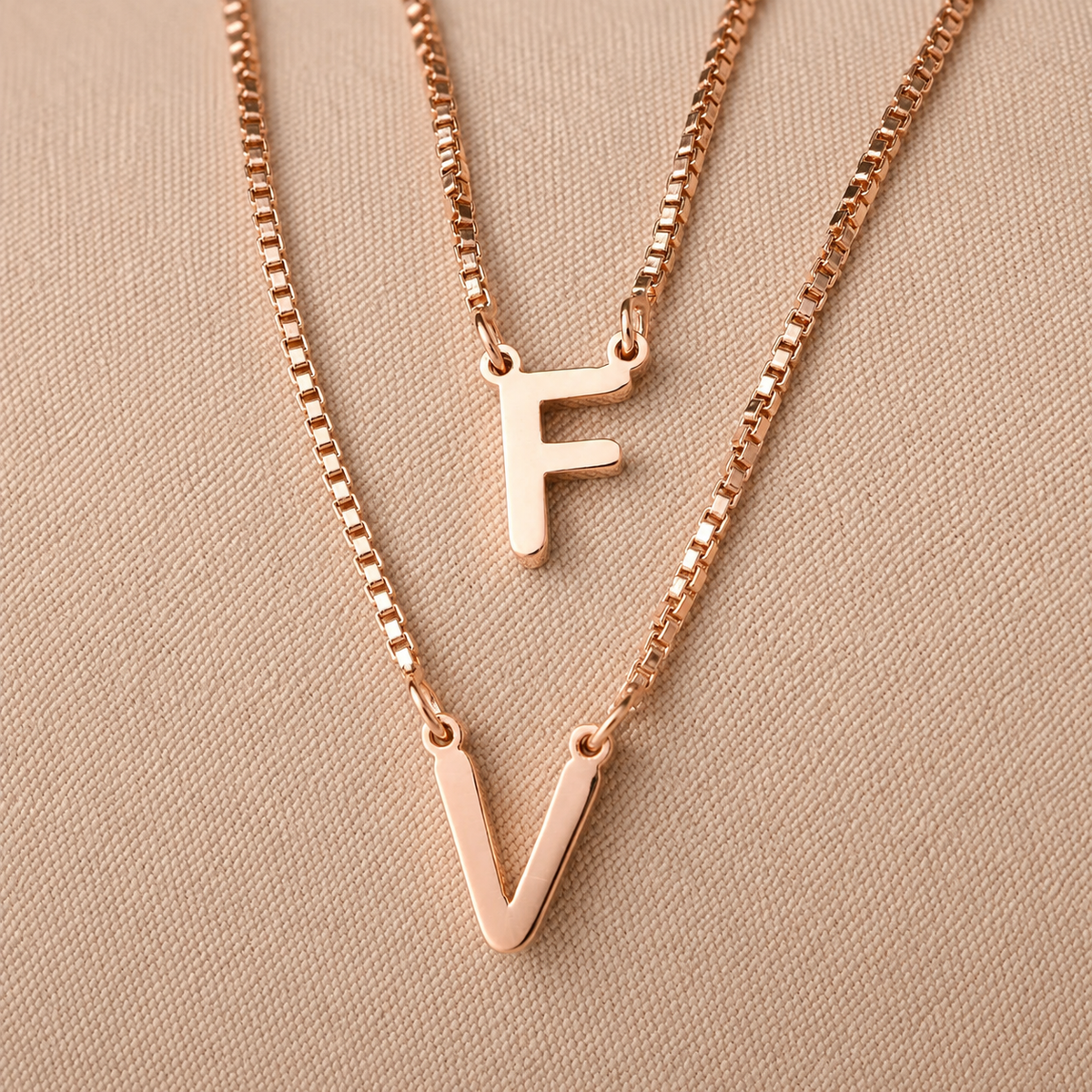 Rose gold necklaces with 'F' and 'V' pendants on a beige background