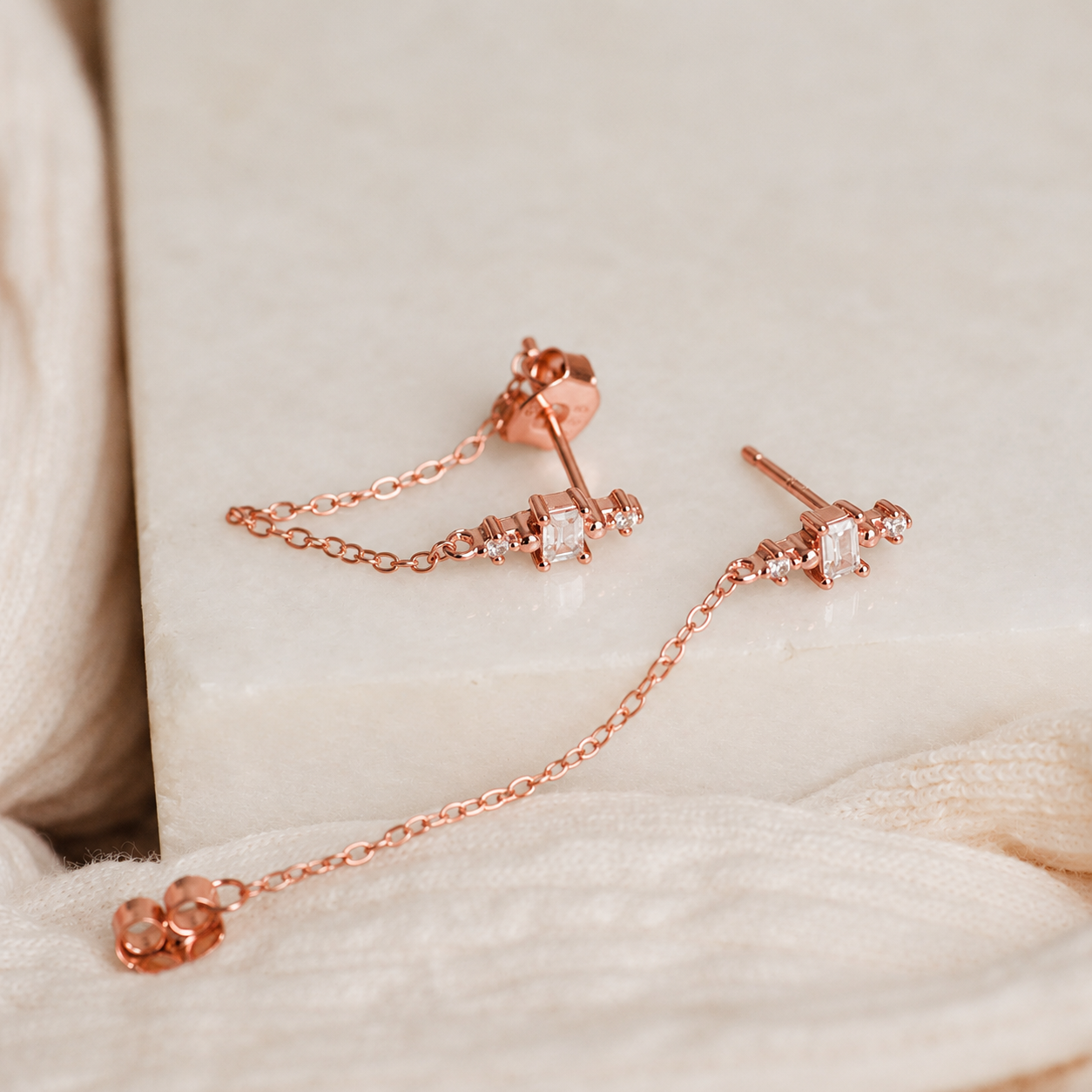 Rose gold earrings with chain detail on a soft fabric background