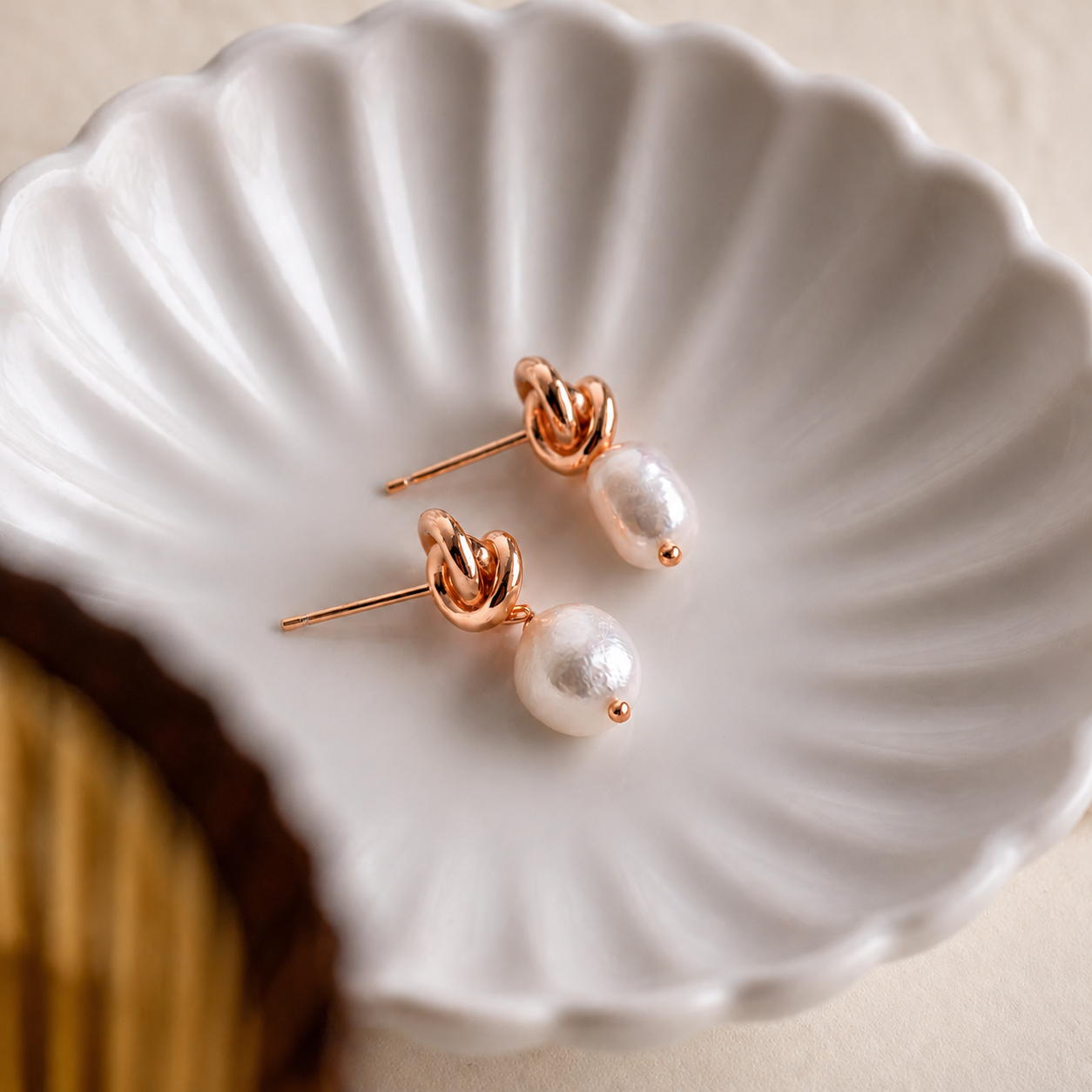 Pearl earrings with rose gold posts on a white shell-shaped dish.