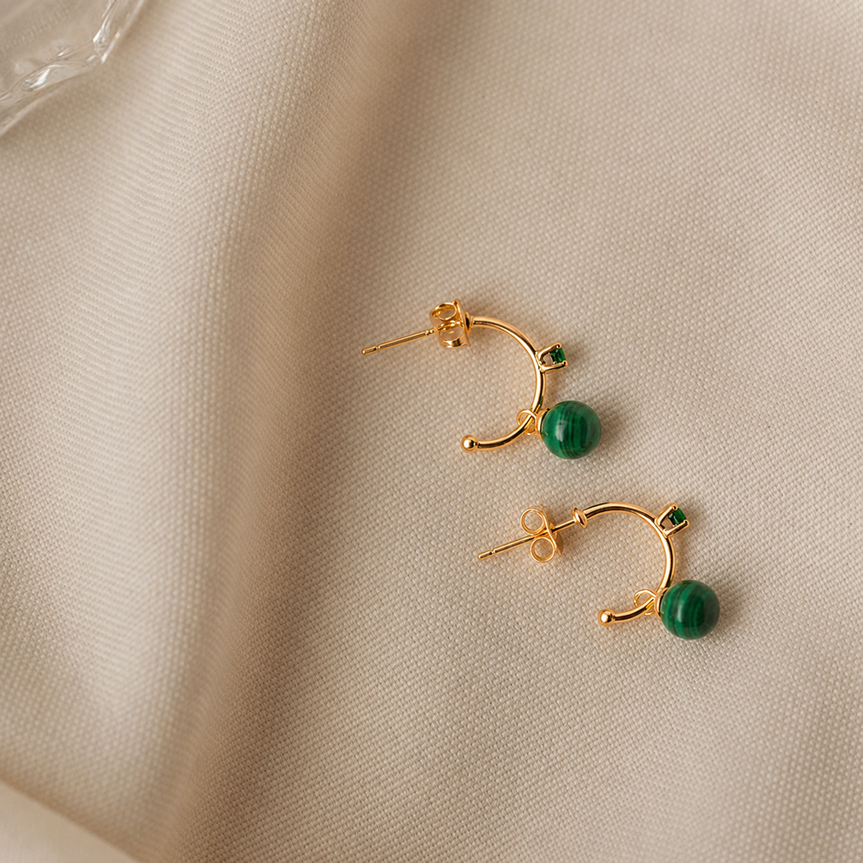Gold earrings with green gemstones on a beige fabric background
