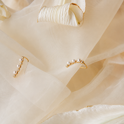 Gold ear cuffs with pearls on a soft beige fabric background
