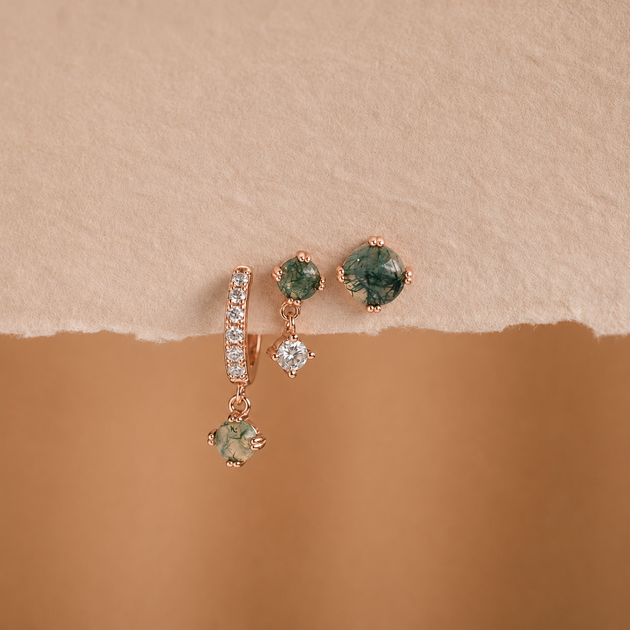 Pair of earrings with green gemstones and rose gold accents on a beige background