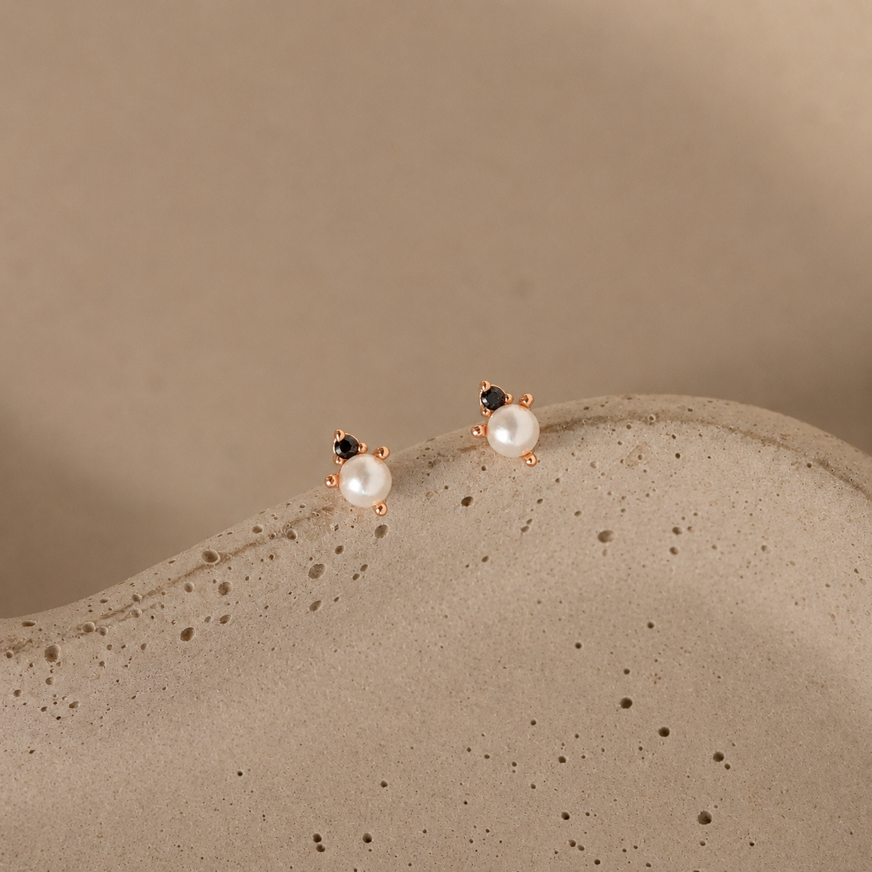 Pair of pearl earrings on a textured beige surface with a neutral background