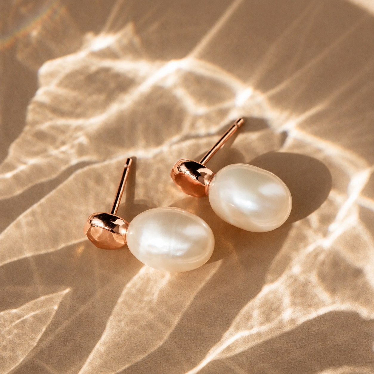 Pearl earrings with rose gold posts on a textured beige surface