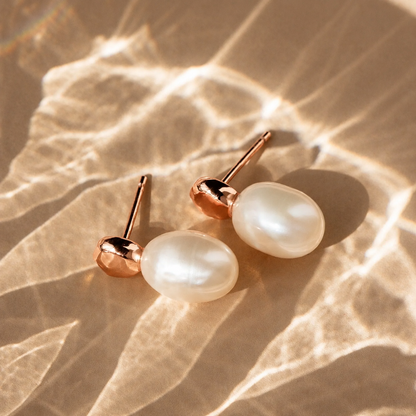 Pearl earrings with rose gold posts on a textured beige surface