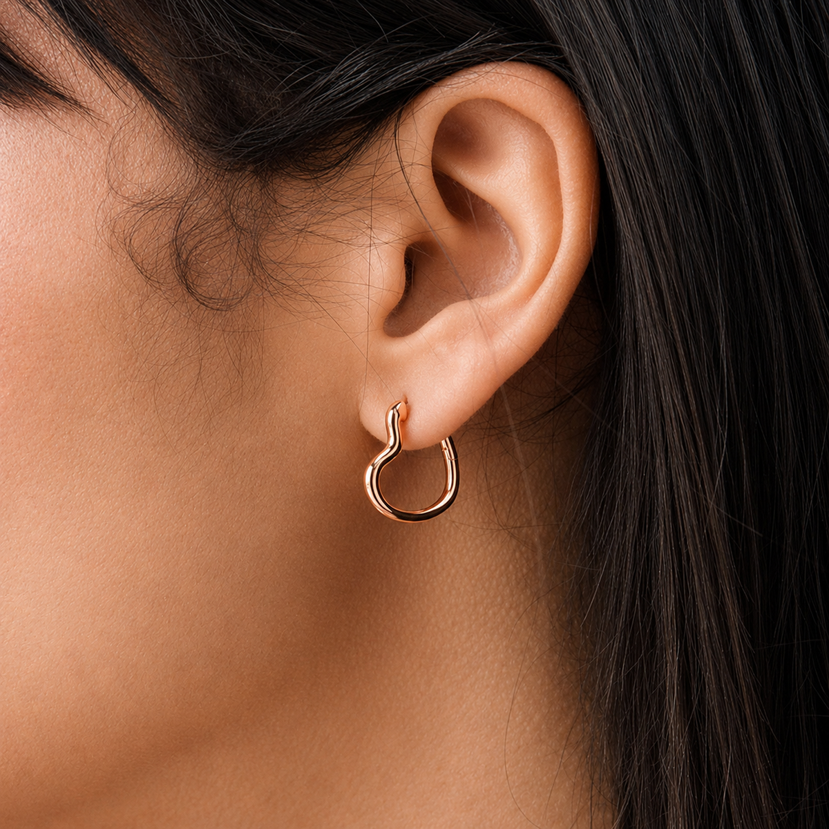 Close-up of an ear wearing a rose gold hoop earring with dark hair partially visible.