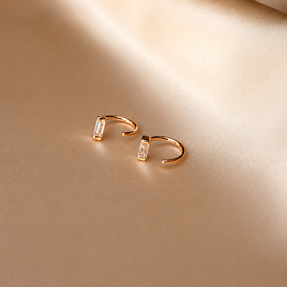 Gold hoop earrings with embedded stones on a beige background