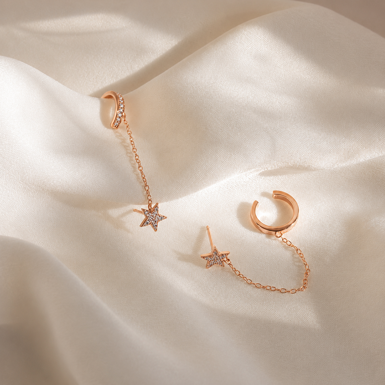 Rose gold dangling hoop earrings with star-shaped charms, displayed on draped cream satin fabric.